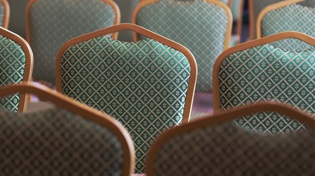 Line of green theater chairs demonstrates fabric with fine diamond Tatar pattern. Wooden frames of chairs emphasize detailed pattern of upholstery