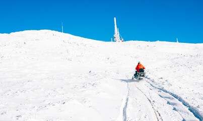 A person riding a snowmobile up a snowy mountain under a vibrant blue sky. Perfect winter adventure scene with untouched snow and clear weather showcasing alpine exploration