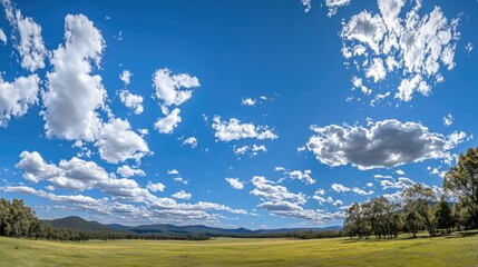 Vibrant panorama showcasing a brilliant blue sky dotted with soft, fluffy white clouds drifting above a lush green landscape.