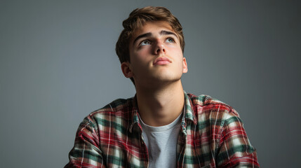Obraz premium Young man in plaid shirt looking thoughtfully upward