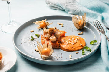 A gourmet scallops lunch with carrot puree in Romesco sauce served on a blue plate with fesalis, a...