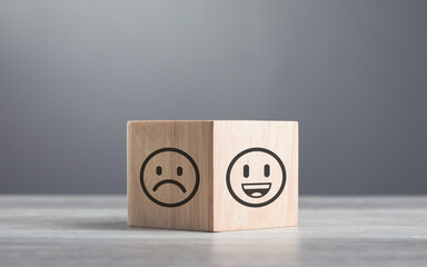Wooden blocks displaying a sad face transitioning to a happy face, symbolizing a shift from negativity to positivity. Final block turns from sad to happy, highlighting the power of a positive outlook