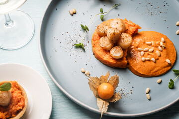 A gourmet scallops lunch with carrot puree in Romesco sauce served on a blue plate with fesalis, a...