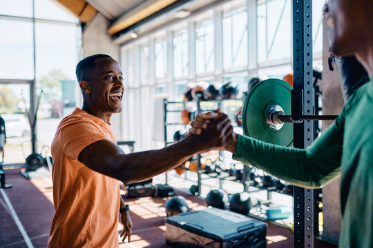 Two diverse young men in sportswear ecstatically shaking hands together after a workout session in a gym