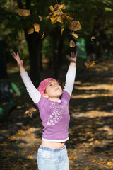 Cute little girl in autumn park playing with leaves