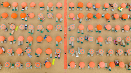Perpendicular aerial view of a beach club with orange umbrellas and people on vacation. The coast is sandy. © Stefano Tammaro