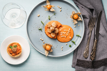 Scallops with carrot puree with Romesco sauce, fesalis and pine nuts on a blue plate on a light...