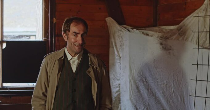 A spy dressed in a classic trench coat gives a briefing in a abandoned hide out during world war 2
