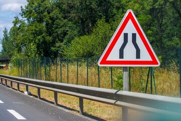 Roadway narrowing sign amidst greenery in Dordogne France roadway