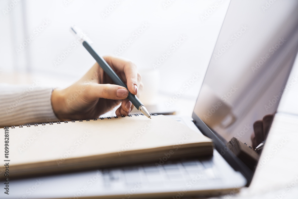 Aufkleber close perspective of a woman's hand making entries in a notepad on a cutting-edge laptop, with a sof