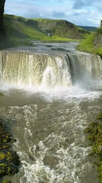Beautiful river forming a waterfall among green grassy mountains in Iceland, Vertical Video.