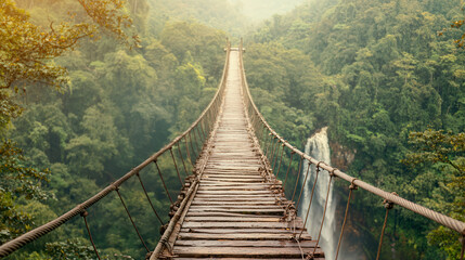 Fototapeta premium Suspended bridge over lush greenery and a waterfall in a serene environment.