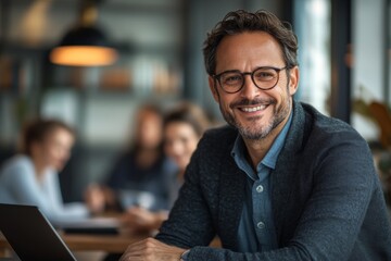 Obraz premium A man wearing glasses and a gray jacket is smiling and holding a laptop