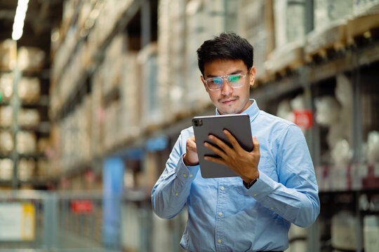 A man wearing glasses and a blue shirt is talking on a cell phone while holding a tablet. 