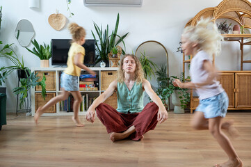 Mature woman meditating with daughters running in living room at home