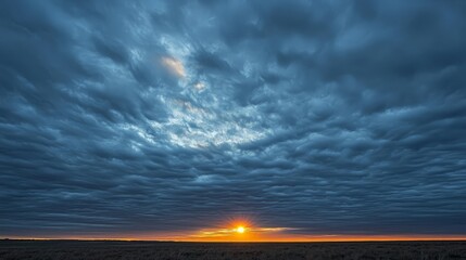 Obraz premium Dramatic sunset with dark, textured clouds over flat landscape.