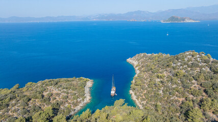 Obraz premium A gulet ship anchored in crystal-clear waters, surrounded by lush green hills and a serene coastal landscape.