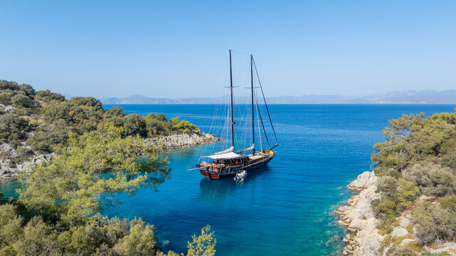 A gulet ship anchored in crystal-clear waters, surrounded by lush green hills and a serene coastal landscape.
