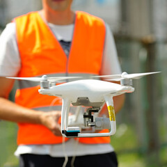 pro quadcopter with camera aboard flying, operator controlling it on the background