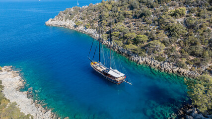 Obraz premium A gulet ship anchored in crystal-clear waters, surrounded by lush green hills and a serene coastal landscape.
