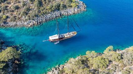 A gulet ship anchored in crystal-clear waters, surrounded by lush green hills and a serene coastal...