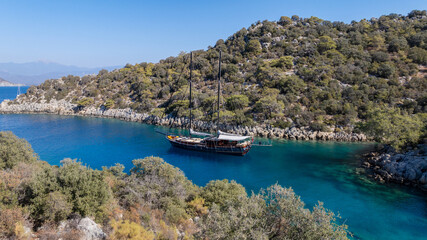 Fototapeta premium A gulet ship anchored in crystal-clear waters, surrounded by lush green hills and a serene coastal landscape.
