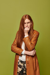 Emotional expression of a young man with long red hair against a vibrant green backdrop