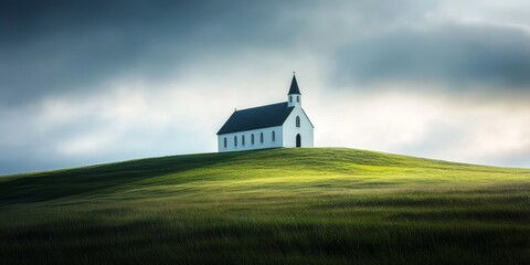 Fototapeta premium A serene white church sits atop a grassy hill, captured in a long exposure photograph on a partially clouded day, showcasing the beauty of the church against the tranquil landscape.