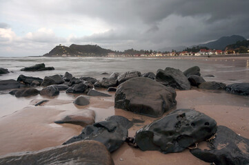 A tranquil rocky beach at dusk with soft waves and an overcast sky