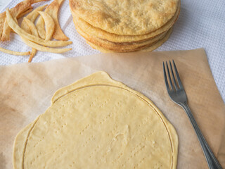 Raw layer rolled out on a baking paper, pierced with fork, pile of baked thin buttery layers, and dough scraps on a white waffle towel ready for cooking of a shortcrust puff pastry Napoleon cake.