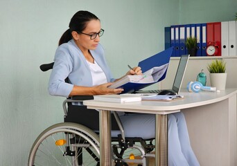 A woman in a wheelchair sits at a desk, reading documents concept