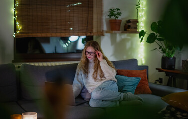 Obraz premium A young woman sitting comfortably on a couch using a laptop during a cozy and festive evening at home