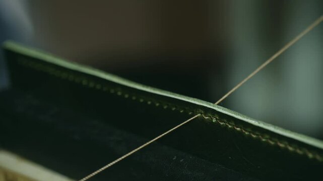 Craftsmanship shines as a skilled artisan stitches high-quality green leather with a needle and thread, showcasing precision and attention to detail in the traditional shoemaking process