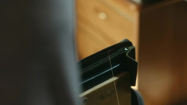 Close-up view of a craftsman meticulously sewing a leather wallet with a needle and thread, showcasing skill and precision in the art of leather repair and restoration