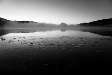 Serene lake view at dawn with misty hills.