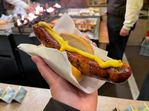 Traditional german grilled roasted sausage bratwurst with mustard in wheat bun in female hand close up on a Christmas market