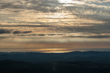 Fototapeta premium dettaglio su varie catene montuose e collinari con la vista che si estende fino al mare adriatico e all'orizzonte, col sole che tramonta dietro alle nuvole