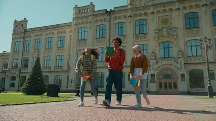 Three multiracial students girls African American women Caucasian female ladies boy man guy male leave college university high school talking walking in city throwing books celebrate education break