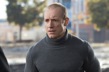 Serious man in gray turtleneck engages in conversation outdoors