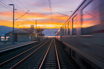 Obraz premium Train speeds past a scenic station at sunset, highlighting the beauty of the landscape and railways
