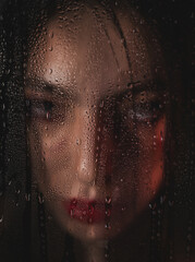 The girl looks aggressively through the glass with raindrops on it