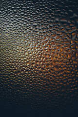Close-up of textured glass with water droplets, highlighted by warm orange lighting, creating an...