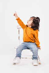 Little girl sitting on a chair points to the sky with a surprised expression