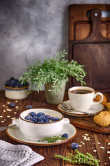 Oatmeal with milk and blueberries and a cup of black coffee on an old wooden table