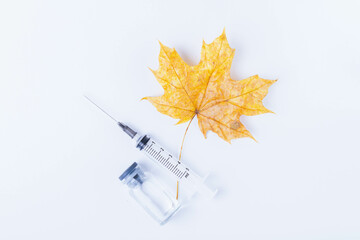 Autumn maple leaf and syringe with vaccine on white background. Vaccination against colds..
