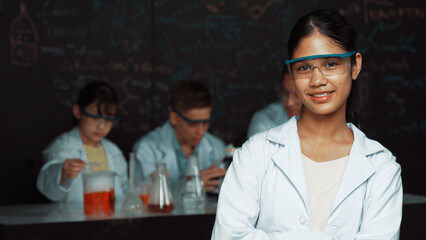 Girl looking at camera with arm folded while people doing experiment at laboratory. Cute student...