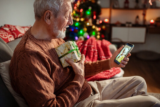 Senior man video calling wife while holding Christmas gift at home