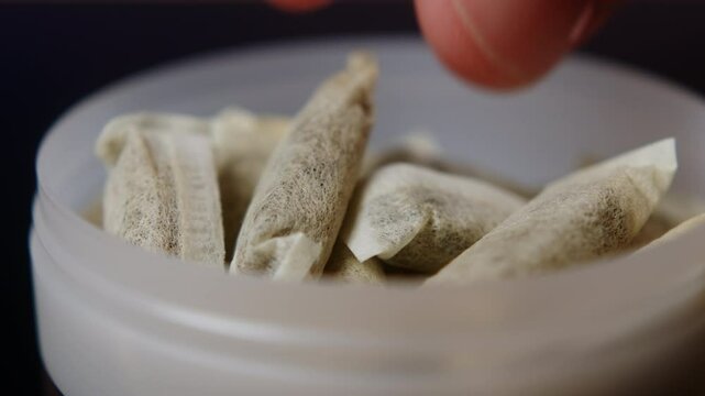 Snus nicotine tobacco close up, pack of tobacco for gum. unhealthy addiction. Man opening box with snus and taking one. 