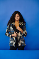 Naklejka premium Striking portrait of a beautiful woman in a stylish jacket against a vivid blue backdrop