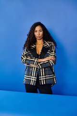 Confident woman in stylish checkered blazer posing against a vibrant blue background
